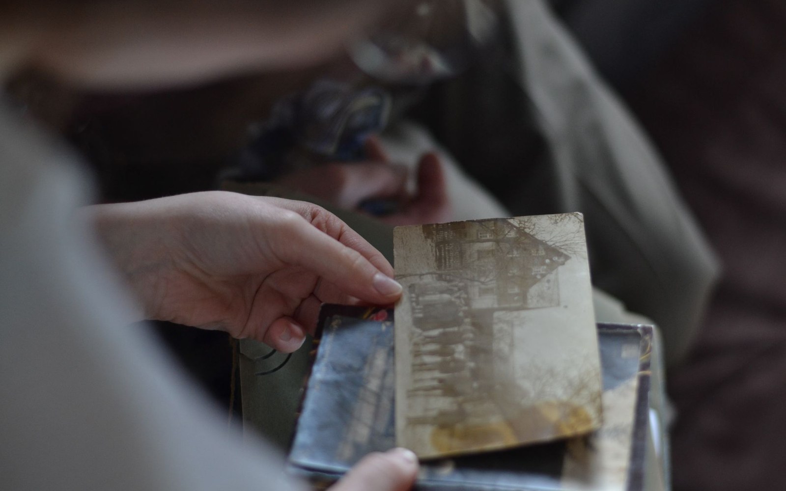 A hand holds a faded sepia-toned photograph of an old building above a stack of similar prints