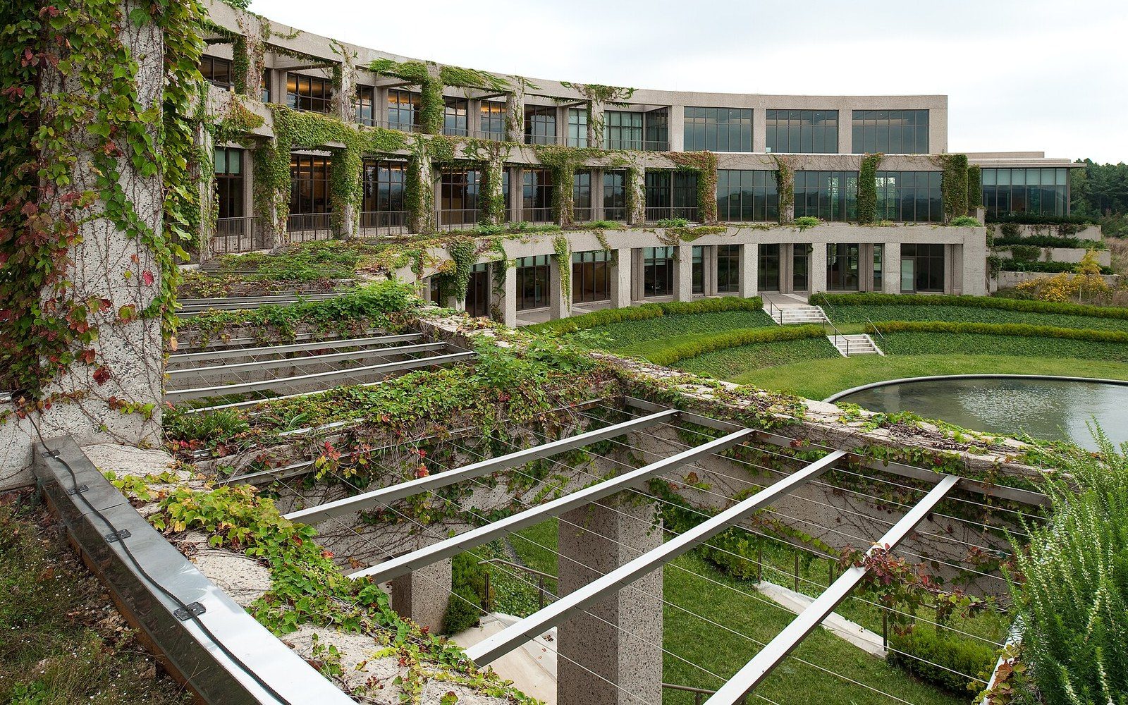 Curved ivy-covered building with terraced gardens and a circular pond in the courtyard