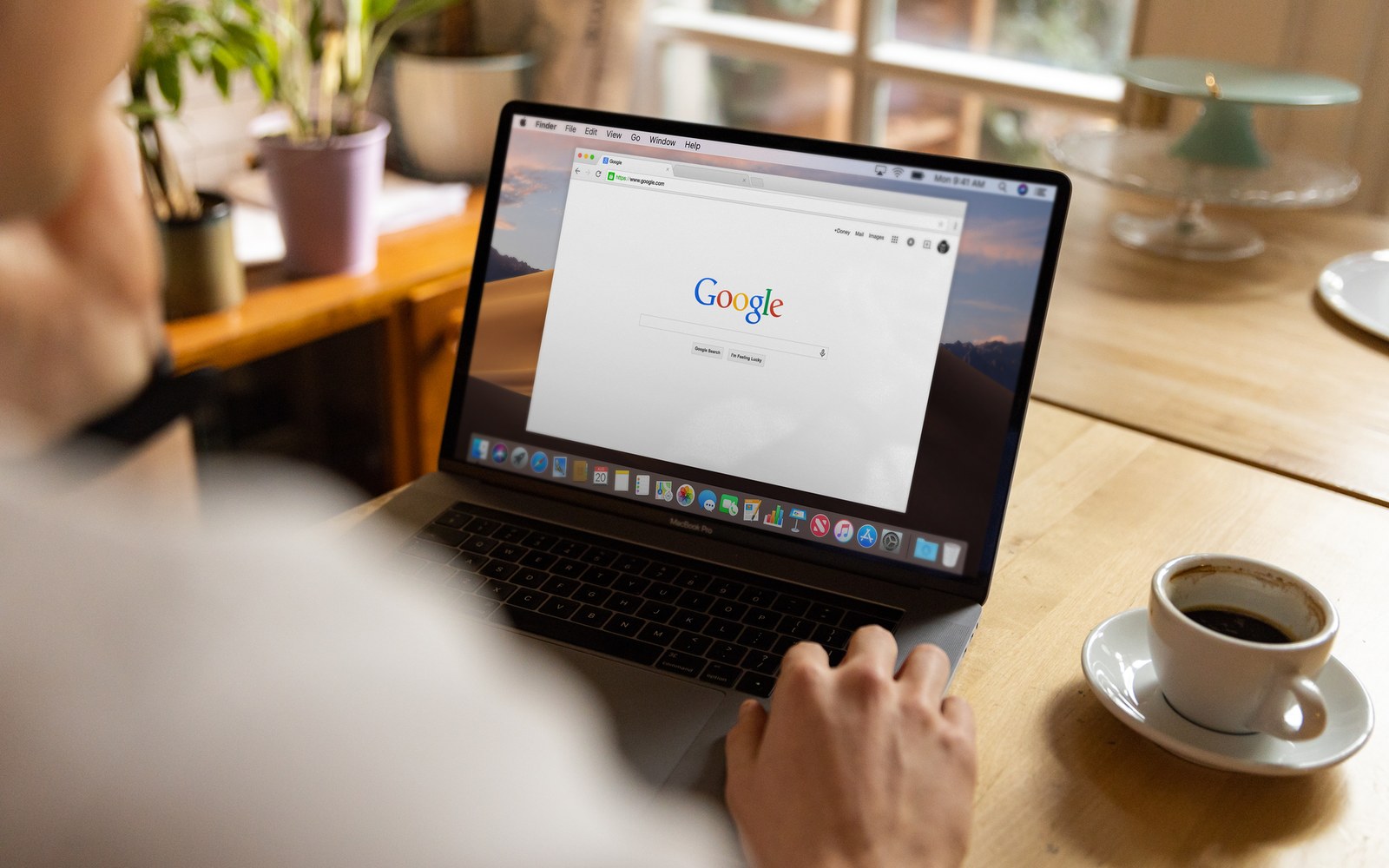 Person browsing the Google homepage on a laptop next to a cup of coffee