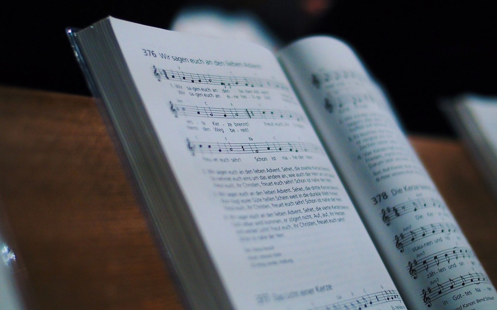 Open German hymnals with printed sheet music resting on a wooden pew